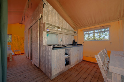 Interieur van een sfeervolle safaritent met houten vloer, keuken en eettafel in Holiday Park Hunzedal.