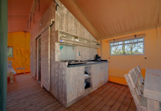 Innenansicht eines komfortablen Safari-Zeltes mit Holzboden, Küchenzeile und Esstisch im Holiday Park Hunzedal.