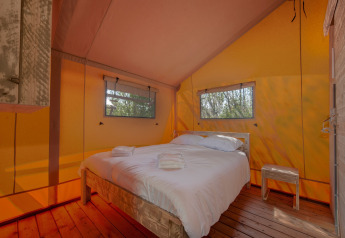 Interior de tienda tipo safari con cama doble y suelo de madera en Holiday Park Hunzedal, Países Bajos.