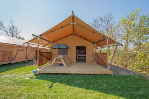 Safari tent at Holiday Park Hunzedal 17 in the Netherlands with a wooden terrace, picnic table, and umbrella.