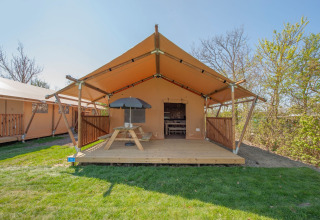 Safari-Zelt im Holiday Park Hunzedal 17 in den Niederlanden mit Holzterrasse, Picknicktisch und Sonnenschirm.