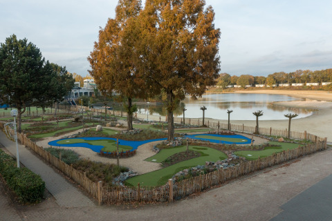 Minigolfbaan naast meer en zandstrand bij Holiday Park «Hunzedal 17» in Nederland, omringd door bomen.