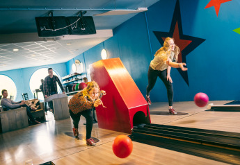 To personer bowler indendørs i farverig bane med stjerner på væggen i Holiday Park Hunzedal 17, Holland.