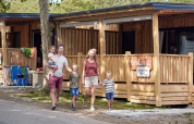 Famiglia davanti a SunLodge Mobile Home Katsura al campeggio Pra'delle Torri in Italia, lodge di legno nello sfondo.