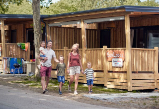 Famiglia davanti a SunLodge Mobile Home Katsura al campeggio Pra'delle Torri in Italia, lodge di legno nello sfondo.