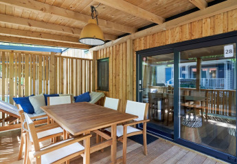 Terraza cubierta de madera con mesa de comedor y zona lounge en SunLodge Mobile Home Katsura, Italia.