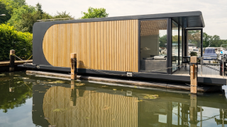 Modernes Hausboot mit Holzverkleidung und Glaswänden, vor Anker in Lemmer, Friesland, Niederlande.