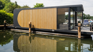 Modernes Hausboot mit Holzverkleidung und Glaswänden, vor Anker in Lemmer, Friesland, Niederlande.