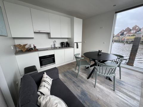 Intérieur moderne de péniche avec cuisine, table à manger, canapé et grande fenêtre sur l'eau.