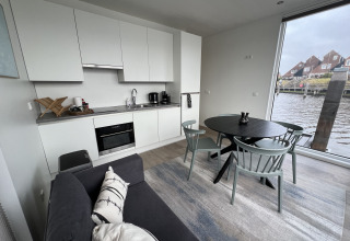 Interior moderno de casa flotante con cocina, mesa de comedor, sofá y gran ventana al agua.