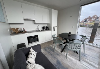Intérieur moderne de péniche avec cuisine, table à manger, canapé et grande fenêtre sur l'eau.