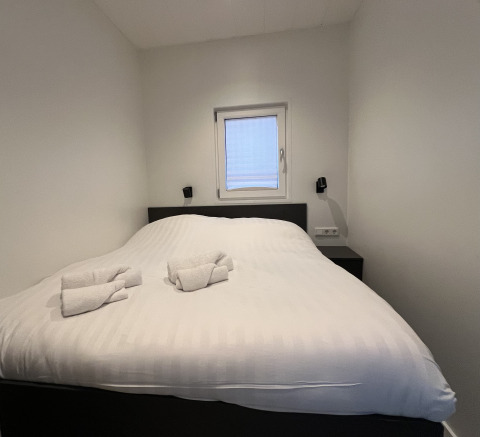 Dormitorio moderno en un houseboat en Lemmer, Países Bajos, con cama doble y toallas blancas dobladas.