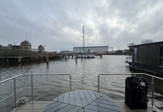 Vista desde una casa flotante en Marina Lemmer, Países Bajos, con mesa, barandilla y barcos en el agua bajo cielo nublado.