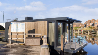 Moderne husbåd ved marinaen Lemmer i Holland, fortøjet ved kajen med udendørs siddeplads og vandudsigt.