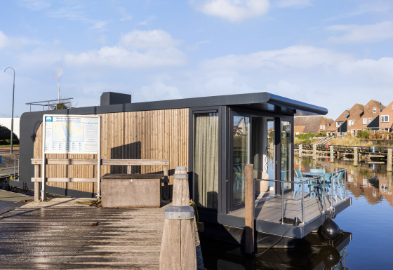 Moderne husbåd ved marinaen Lemmer i Holland, fortøjet ved kajen med udendørs siddeplads og vandudsigt.