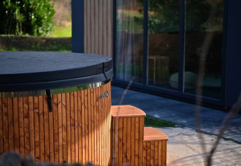 Jacuzzi redondo de madera con tapa negra y escalera junto a cabaña en el camping De Witte Berg, Países Bajos.