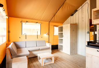Licht interieur van safari-tent Nomad op Camping Vilanova Park in Spanje met bank, tafel en kast.
