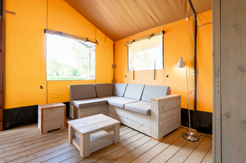 Interno della tenda safari Nomad con divano in legno e arredo moderno al campeggio Vilanova Park, Spagna.