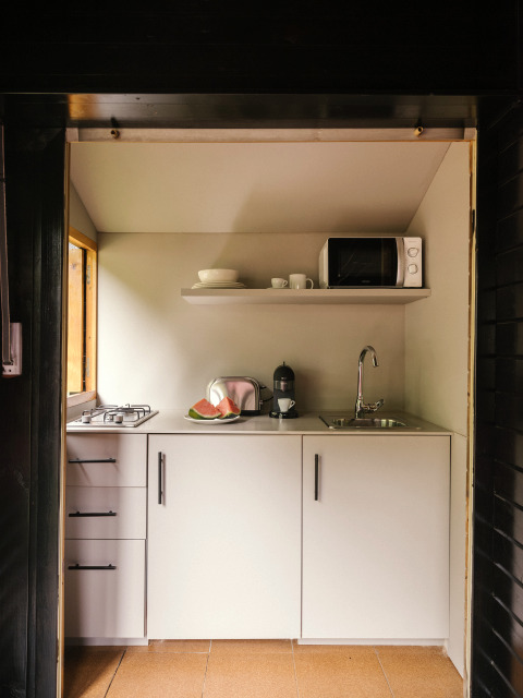 Compact kitchen in Bungalow «Basic Couple» at Wecamp Cudillero, Spain, with stove, sink, and microwave.