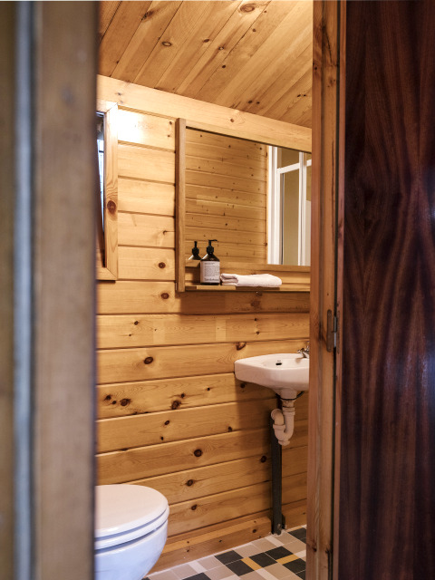 Small bathroom with wood panel walls, mirror, sink, and toilet inside Bungalow Basic Couple at Wecamp Cudillero.
