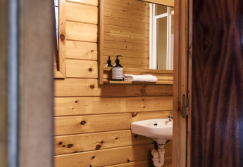 Small bathroom with wood panel walls, mirror, sink, and toilet inside Bungalow Basic Couple at Wecamp Cudillero.