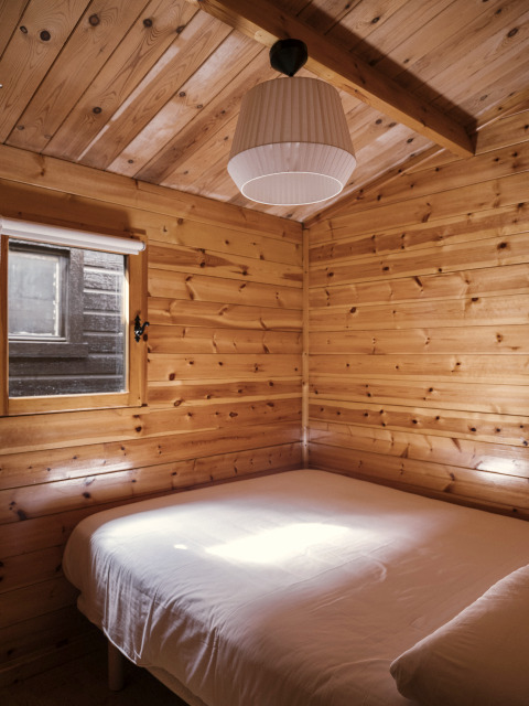 Holzverkleidetes Schlafzimmer mit Doppelbett und Fenster in Bungalow Basic Family Plus bei Wecamp Cudillero, Spanien.