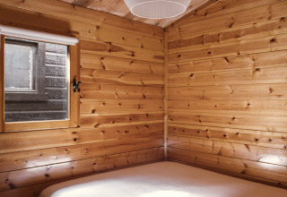 Holzverkleidetes Schlafzimmer mit Doppelbett und Fenster in Bungalow Basic Family Plus bei Wecamp Cudillero, Spanien.