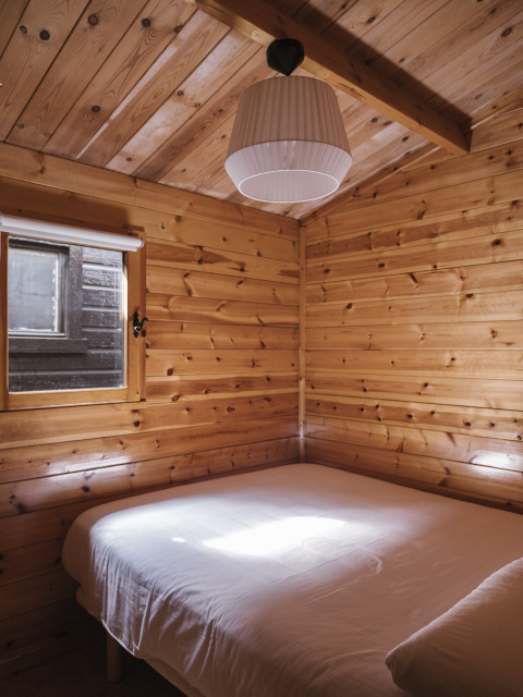 Dormitorio de madera acogedor con cama doble y ventana en Bungalow Basic Family Plus de Wecamp Cudillero, España.