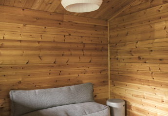 Holzverkleideter Glamping-Raum mit grauem Sofa, modernem Lampenschirm und schwarzem Tisch.