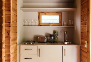 Kleine Küchenzeile in einer Holzhütte mit weißen Schränken, Toaster, Kaffeemaschine und Ananas.