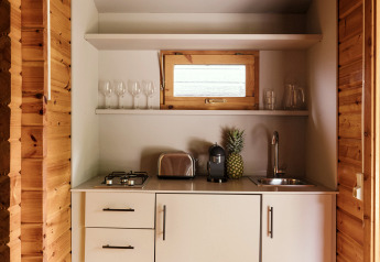 Kleine Küchenzeile in einer Holzhütte mit weißen Schränken, Toaster, Kaffeemaschine und Ananas.
