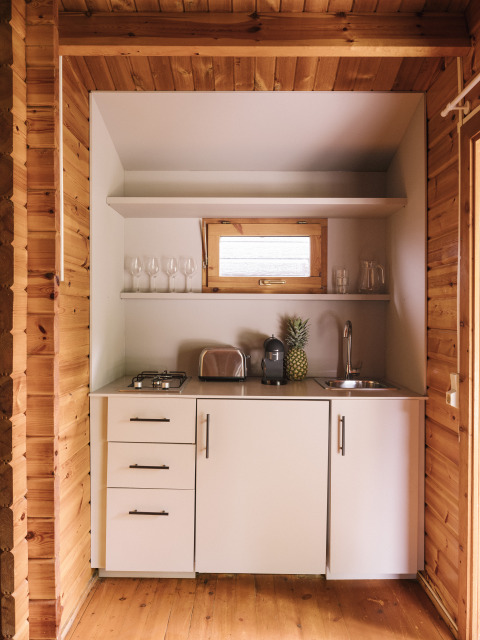 Pequeña cocina en cabina de madera con armarios blancos, tostadora, cafetera y una piña fresca.