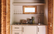 Pequeña cocina en cabina de madera con armarios blancos, tostadora, cafetera y una piña fresca.