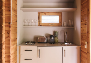 Pequeña cocina en cabina de madera con armarios blancos, tostadora, cafetera y una piña fresca.