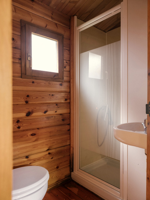 Kleine badkamer met houten wanden, douche, toilet en lavabo, zoals vaak bij glamping verblijf.