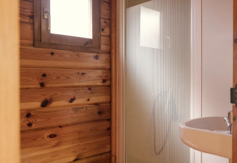 Kleines Badezimmer mit Holzwänden, Toilette, Dusche und Waschbecken in einer Glamping-Unterkunft.