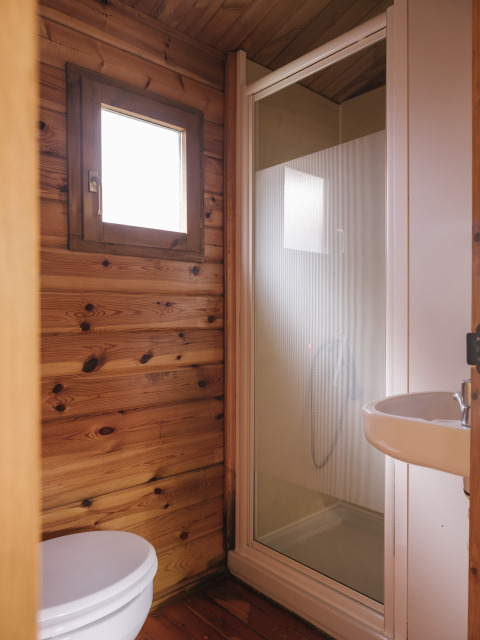 Baño pequeño con paredes de madera, ducha, inodoro y lavabo, ideal para alojamiento glamping.