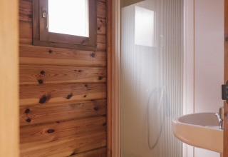 Baño pequeño con paredes de madera, ducha, inodoro y lavabo, ideal para alojamiento glamping.