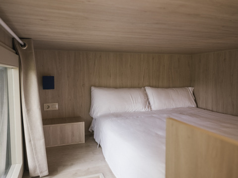 Gezellige slaapkamer in Tiny Home «Family Wood» bij Wecamp Cudillero, Spanje, met licht houten interieur.