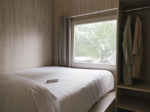 Lichte slaapkamer met dubbel bed, groot raam en kleerkast in Tiny Home «Family Wood» bij Wecamp Cudillero, Spanje.