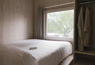 Lichte slaapkamer met dubbel bed, groot raam en kleerkast in Tiny Home «Family Wood» bij Wecamp Cudillero, Spanje.