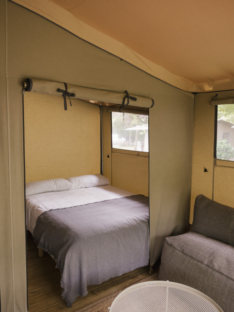 Intérieur d’une tente safari avec lit double, canapé et fenêtres au Cottage Family Tent de Wecamp Cudillero, Espagne.