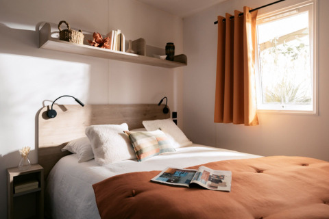 Gezellige slaapkamer met dubbel bed en oranje gordijnen in Next L Titania bij Trasimeno Glamping Resort, Italië.
