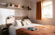 Camera accogliente con letto matrimoniale e tende arancioni al Next L Titania del Trasimeno Glamping Resort, Italia.