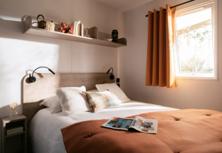 Gezellige slaapkamer met dubbel bed en oranje gordijnen in Next L Titania bij Trasimeno Glamping Resort, Italië.