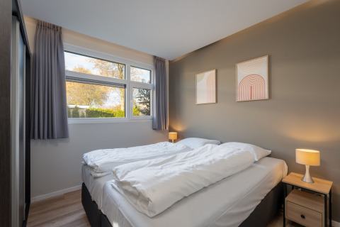 Slaapkamer in Forest lodge bij vakantiecentrum 't Schuttenbelt, Nederland, met tweepersoonsbed en raam.