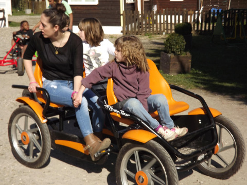 A woman and two children enjoy a sunny pedal kart ride at Flower Camping de la Trye, Hauts-de-France, France.