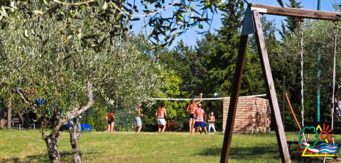 Vakantiepark met mensen die volleyballen op het gras, schommel en bomen bij Centro Vacanze San Marino.