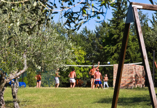Feriepark med folk der spiller volleyball på græsplæne, gyngestativ og træer i Centro Vacanze San Marino.