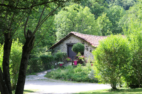 Stone cottage with red tiled roof surrounded by lush greenery at Moulin de Chaules campsite, France.
